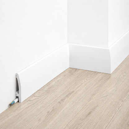 Plinthe décorative blanche MD030 installée le long d’un mur gris avec parquet bois clair, intégrant un canal pour câbles.