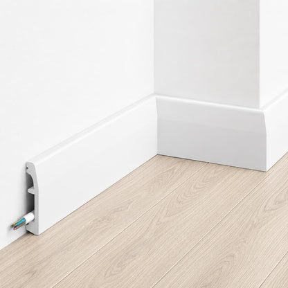 Plinthe décorative blanche MD017 200x6,9x1,4 cm avec cache-câble intégrée posée sur mur gris et sol effet bois Plinthe décorative blanche MD017 200x6,9x1,4 cm avec cache-câble intégrée posée sur mur gris et sol effet bois